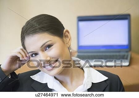 Stock Image - Portrait of a businesswoman smiling with a laptop in the background. Fotosearch