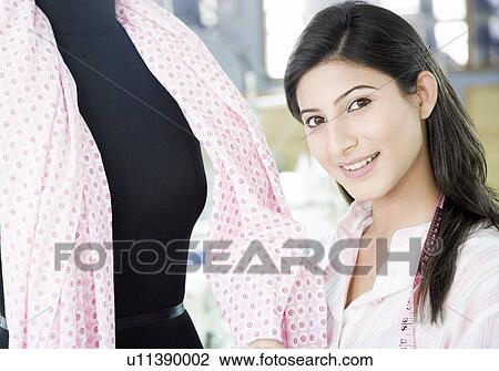Stock Image - Portrait of a female fashion designer smiling near a mannequin. Fotosearch