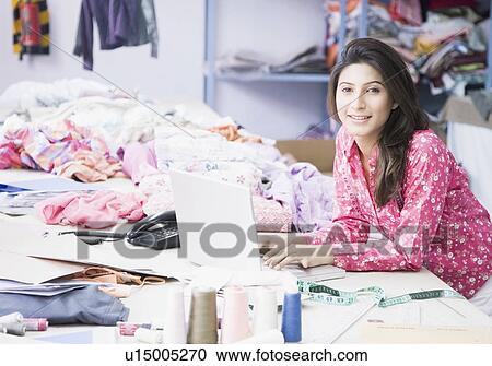 Stock Image - Portrait of a female fashion designer using a laptop and smiling. Fotosearch