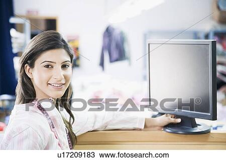 Stock Image - Portrait of a female fashion designer smiling in front of a computer monitor. Fotosearch