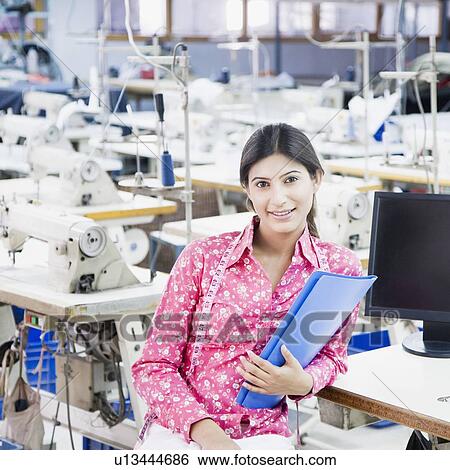 Portrait of a female fashion designer holding a file in a textile industry and smiling View Large Photo Image Stock Photograph - Portrait of a female fashion designer holding a file in a textile industry and smiling. Fotosearch