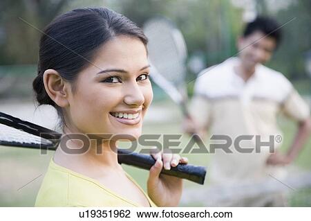 Stock Image - Portrait of a young woman holding a tennis racket and smiling. Fotosearch