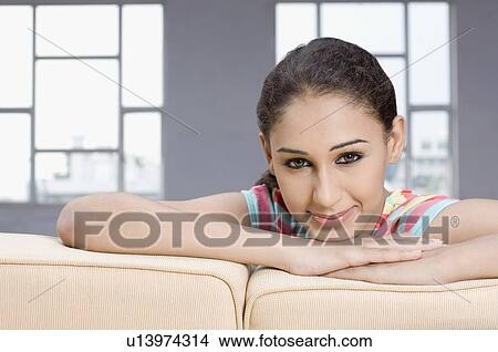 Picture - Portrait of a young woman sitting on a couch and smirking. Fotosearch