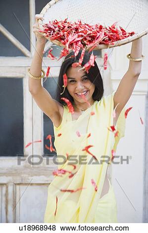 Stock Photo - Portrait of a young woman spraying red chili peppers from a tray. Fotosearch