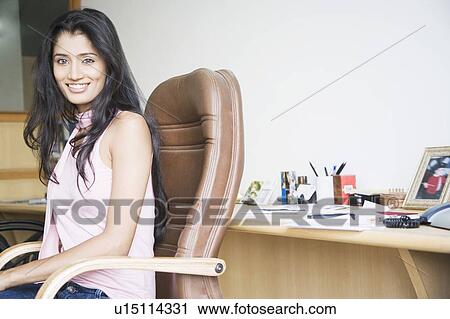Stock Image - Side profile of a businesswoman sitting on an office chair and smiling. Fotosearch