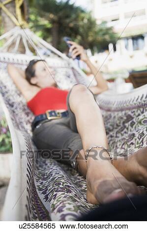Young woman lying in a hammock and holding a mobile phone View Large Photo Image Stock Photography - Young woman lying in a hammock and holding a mobile phone. Fotosearch