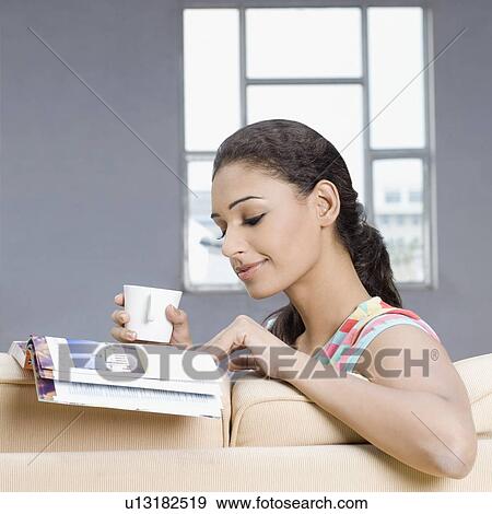 Young woman sitting on a couch and reading a magazine View Large Photo Image Stock Photo - Young woman sitting on a couch and reading a magazine. Fotosearch