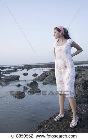Stock Image - Young woman standing on the beach and thinking. Fotosearch