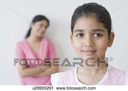 Stock Image - Close-up of a girl smirking with a mid adult woman standing in the background. Fotosearch