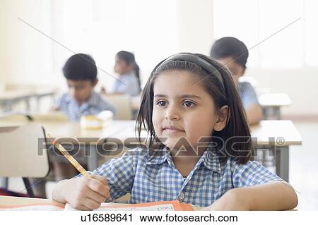 Stock Image - Close-up of a schoolgirl sitting at a desk with other students in the background. Fotosearch