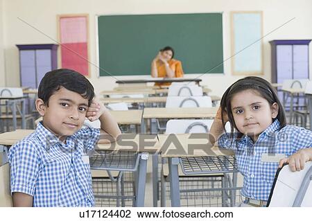 Close-up of two students sitting in a classroom with their teacher sitting in the background View Large Photo Image Stock Image - Close-up of two students sitting in a classroom with their teacher sitting in the background. Fotosearch