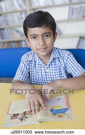 Stock Image - Portrait of a boy reading a book in a school library. Fotosearch