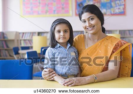 Stock Image - Portrait of a female teacher sitting with a schoolgirl in a library. Fotosearch