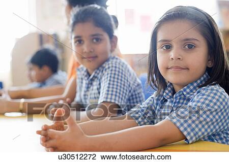 Stock Image - Portrait of a school girl with her classmates and a teacher sitting at a table. Fotosearch