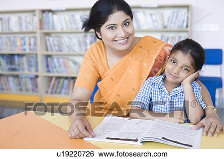 Stock Photograph - Portrait of a school teacher sitting in a library with her student and smiling. Fotosearch