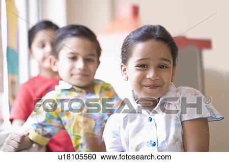 Stock Image - Portrait of a schoolgirl grinning with two schoolboys behind her. Fotosearch