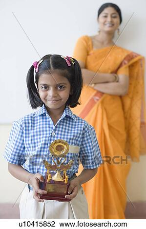Portrait of a schoolgirl holding a trophy with a teacher in the background View Large Photo Image Stock Image - Portrait of a schoolgirl holding a trophy with a teacher in the background. Fotosearch