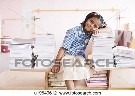 Stock Image - Portrait of a schoolgirl leaning over a stack of books and smiling. Fotosearch