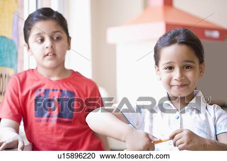 Stock Image - Portrait of a schoolgirl sharpening her pencil and grinning. Fotosearch