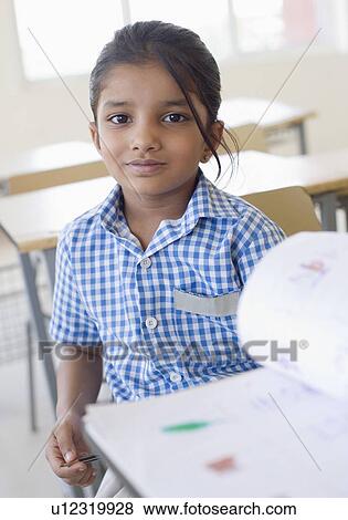 Stock Photo - Portrait of a schoolgirl sitting at a desk with a book in front of her. Fotosearch