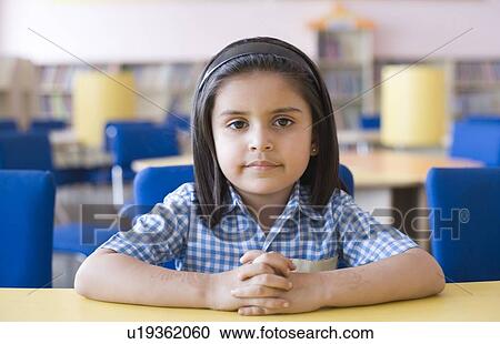 Stock Image - Portrait of a schoolgirl with her hands clasped sitting in a library. Fotosearch