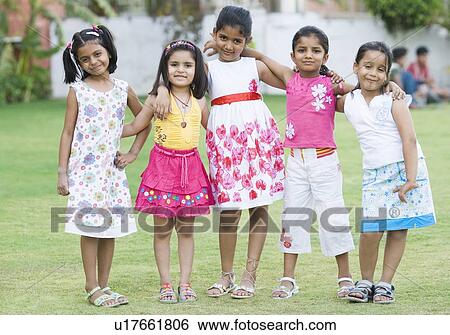 Stock Photograph - Portrait of five girls standing together in a lawn and smiling. Fotosearch