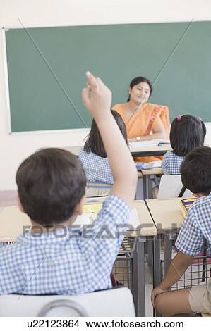 Picture - Rear view of a schoolboy in a classroom with his hand raised. Fotosearch