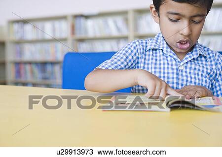 Stock Image - Schoolboy reading a book in a library. Fotosearch