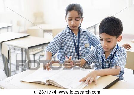 Schoolboy reading a book with a schoolgirl assist him View Large Photo Image Picture - Schoolboy reading a book with a schoolgirl assist him. Fotosearch