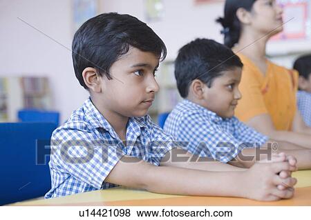 Schoolboys sitting at a desk with their teacher in a library View Large Photo Image Stock Photo - Schoolboys sitting at a desk with their teacher in a library. Fotosearch