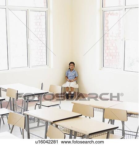 Stock Image - Schoolgirl sitting in the corner of a classroom. Fotosearch
