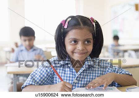 Picture - Schoolgirl writing on a notepad in a classroom and smirking. Fotosearch
