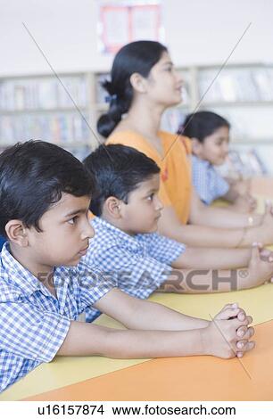 Side profile of a female teacher sitting at a desk with her students in a library View Large Photo Image Picture - Side profile of a female teacher sitting at a desk with her students in a library. Fotosearch