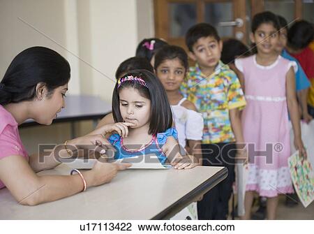 Stock Image - Teacher checking drawings of students in a classroom. Fotosearch