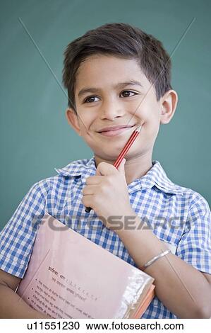 Close-up of a schoolboy holding a pencil and a book in front of a blackboard and smiling View Large Photo Image Stock Image - Close-up of a schoolboy holding a pencil and a book in front of a blackboard and smiling. Fotosearch