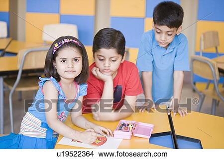 Picture - Portrait of a girl drawing on a sheet of paper with two boys looking at her drawing sheet. Fotosearch