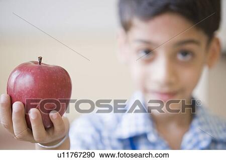 Stock Image - Portrait of a schoolboy holding an apple and smiling. Fotosearch