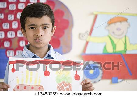 Stock Photo - Portrait of a schoolboy holding his drawing and making a face. Fotosearch