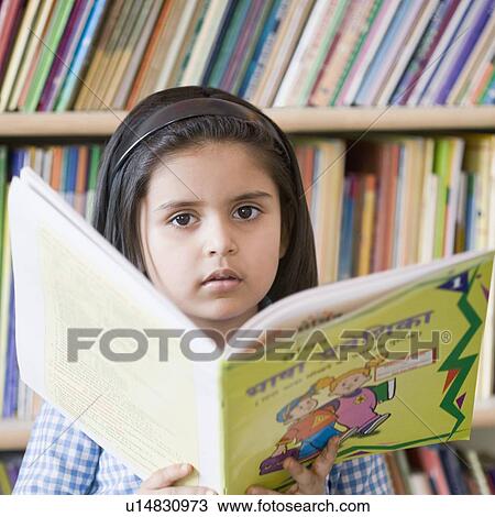 Stock Image - Portrait of a schoolgirl holding a book in a library. Fotosearch