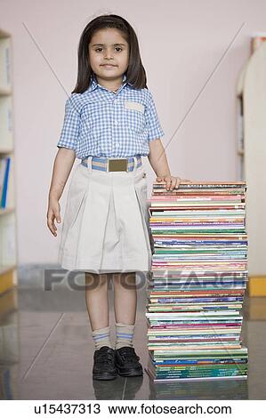 Stock Image - Portrait of a schoolgirl standing near a stack of books. Fotosearch