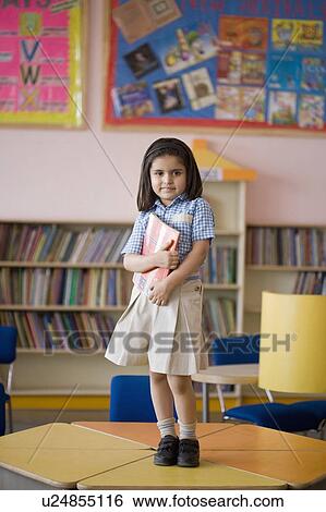 Stock Photograph - Portrait of a schoolgirl standing on table in a library. Fotosearch