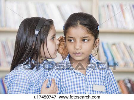 Stock Photo - Side profile of a schoolgirl whispering into her friend's ear. Fotosearch