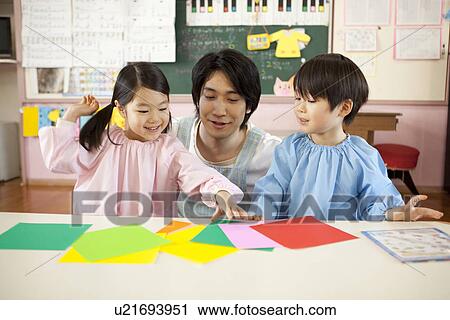 Stock Image - Kindergarten Teacher and Children Playing Origami. Fotosearch