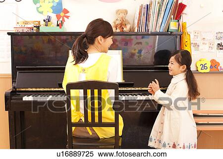Stock Photography - Nursery Teacher Playing Piano with Girl. Fotosearch