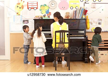 Stock Image - Nursery Teacher Playing Piano with Children. Fotosearch