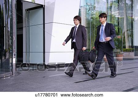 Stock Image - Two businessmen holding briefcase and walking. Fotosearch