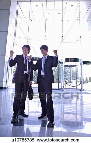 Two businessmen standing together with fists up and smiling View Large Photo Image Stock Photography - Two businessmen standing together with fists up and smiling. Fotosearch