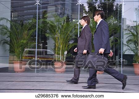 Two businessmen walking and holding briefcase together View Large Photo Image Stock Photograph - Two businessmen walking and holding briefcase together. Fotosearch