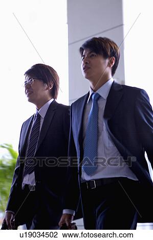 Stock Image - Two businessmen walking and looking away together. Fotosearch