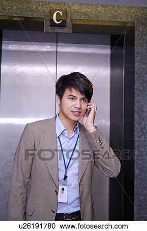 Stock Image - Young businessman holding mobile phone and standing before elevator. Fotosearch